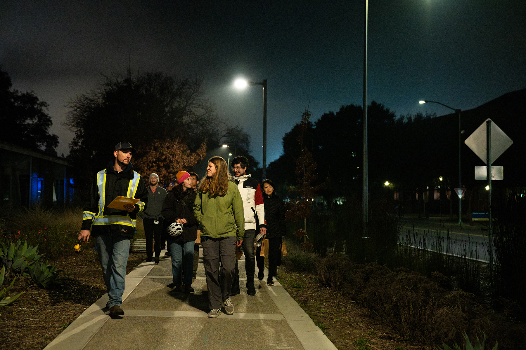 Derek Benson, an electrician with UC Davis Facilities Management, leads a group of people walking together on a lighted pathway at night.
