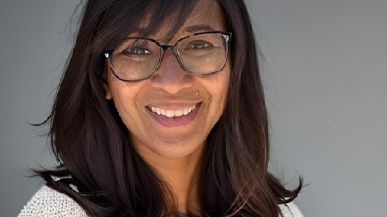 Smiling woman with glasses and shoulder-length dark hair, casual headshot on gray background
