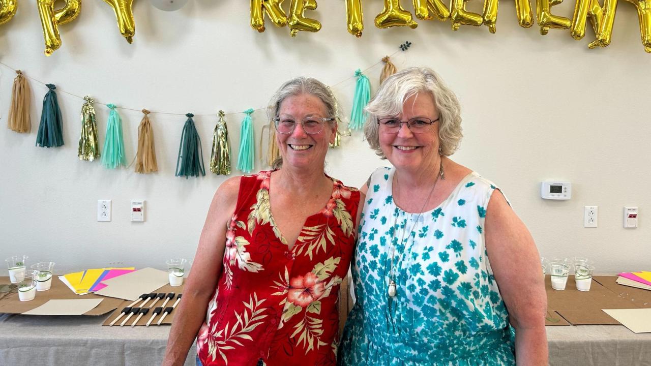 Mary Gibson and Roxanne Loe smiling at their retirement party, with decorations in the background