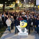 Group photo of UC Davis staff and students outside of the Memorial Union after dark with a cut-out of the Campus Safety Lighting Walk mascot Bulby in front.
