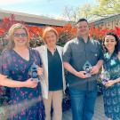 Jennifer Thompson, Aaron Knapek, and Amber Sharpe stand holding awards, posing with Clare Shinnerl