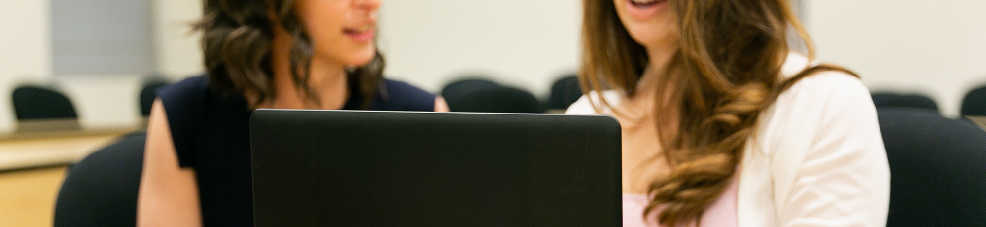 two female employees talking with one another while looking at a laptop